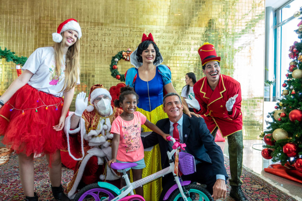 michelle bolsonaro vestida de branca de neve entrega brinquedo para uma criança